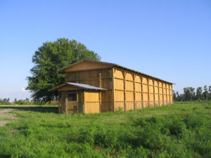 100 by 20 feet flight cage for birds of prey. It's wooden and in he middle of no where with a sunny/blue sky in the background.